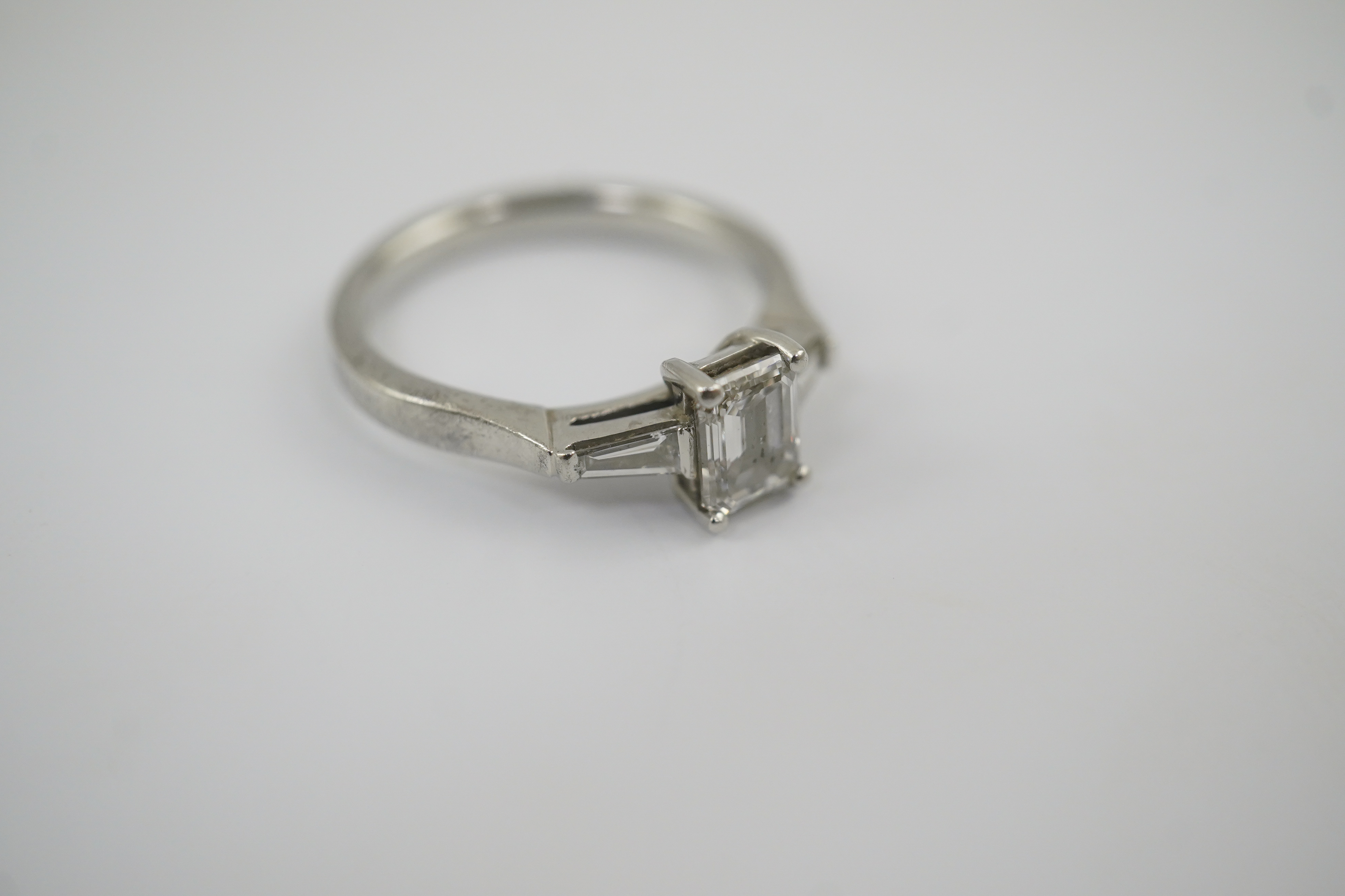 A modern platinum and single stone emerald cut diamond set ring, with two stone tapered baguette cut diamond set shoulders